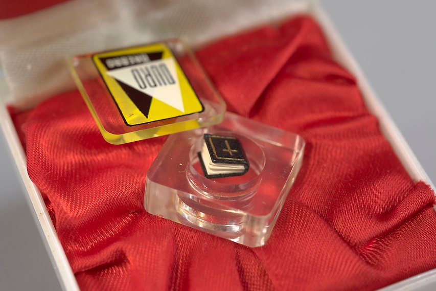 Foto av en miniatyrbok som ligger på en röd sidenkudde i ett smyckesetui.