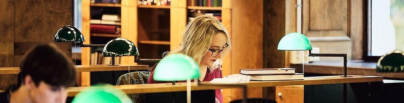 En kvinna sitter i en läsesal i ett bibliotek.
