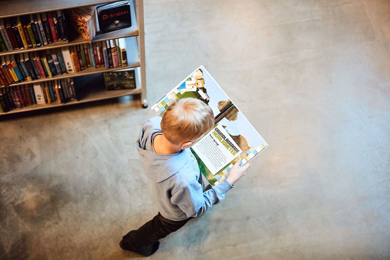 Ett barn går genom ett bibliotek med en Minecraft-bok i händerna.
