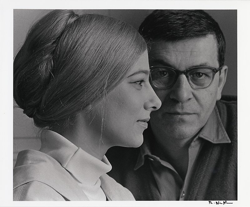 Black and white photograph of a woman in profile and a man looking out from behind her.