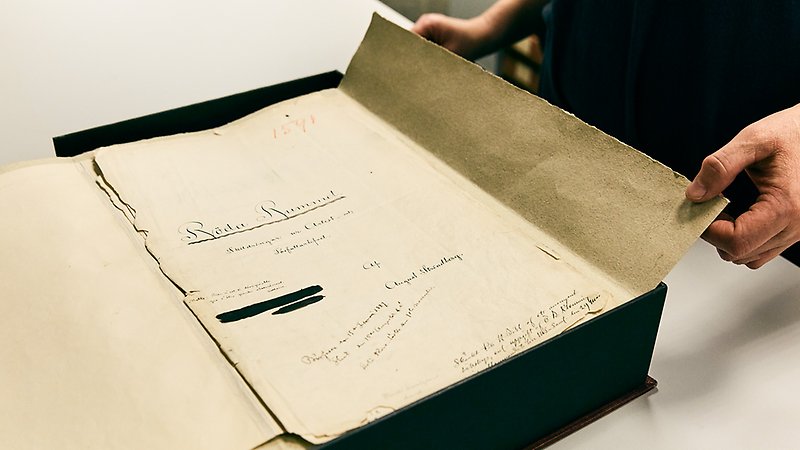 Person som bläddrar i August Strindbergs manuskript till Röda rummet liggandes i en arkivmapp.