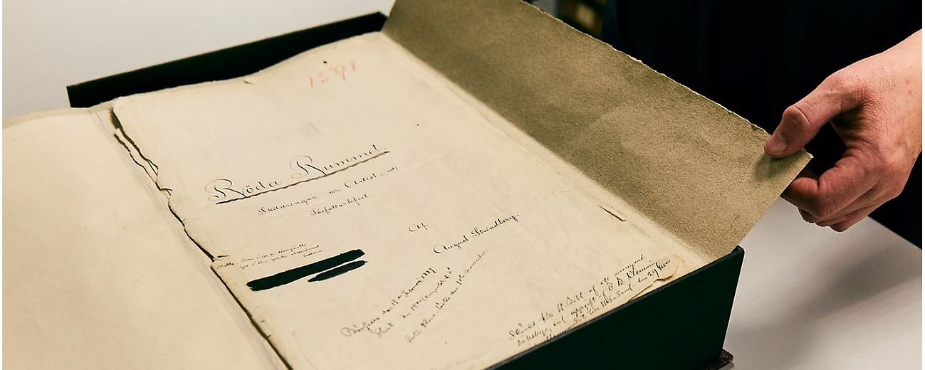Person som håller i manuskriptet till August Strindbergs Röda rummet.