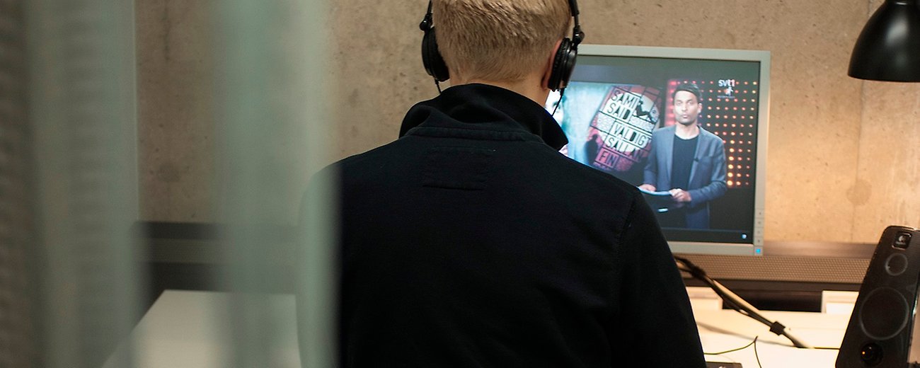 Person med hörlurar sedd bakifrån som tittar på en datorskärm.