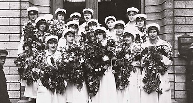 Svartvitt fotografi av studenter med vita mössor och blommor i händerna på en trappa.