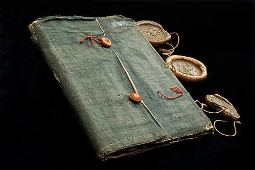 Medeltida mjukt textilband i gråblått linne med tre sigill fästa med snöre vid ryggen. Handskrift, Sverige, 1451-1452.