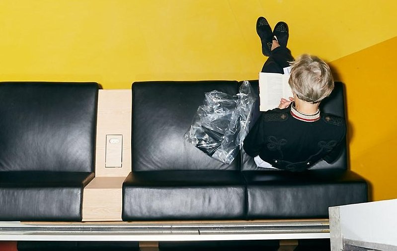 Person som läser en bok sittande på en svart soffa sedd uppifrån.