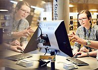 Person framför en dator i biblioteksmiljö.