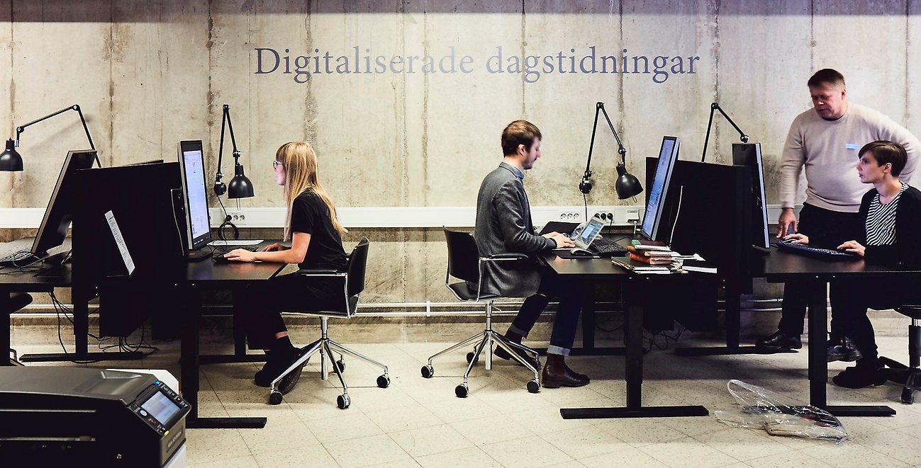 Personer som sitter och står vid datorer.