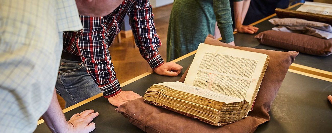 Personer står lutade över en bok. 