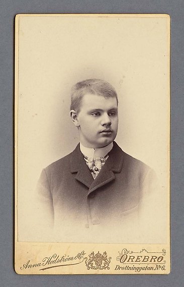 Svartvitt fotografi av kortklippt ung man med vit skjorta och yllekavaj.