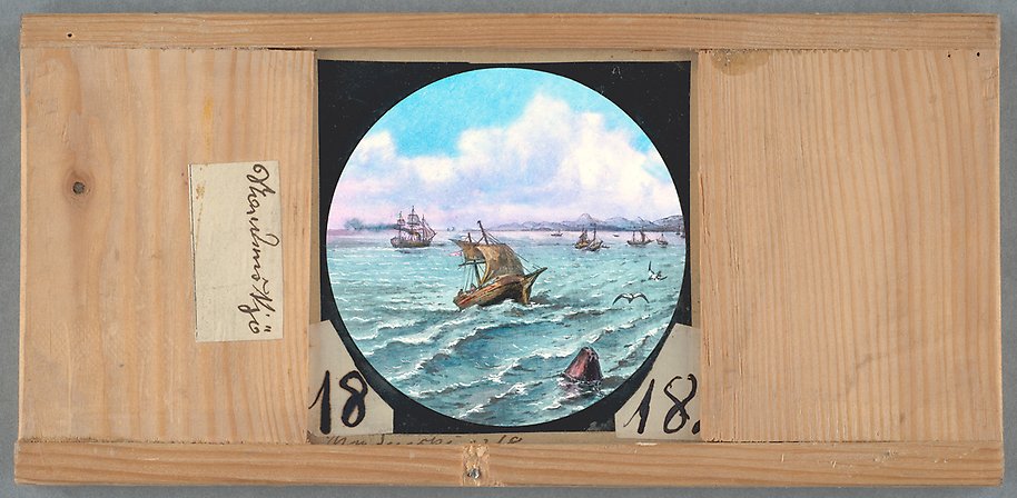 Målning fäst i träram. Vega omgärdat av flera skepp till havs. Sjöfåglar flyger på blå himmel med vita moln.