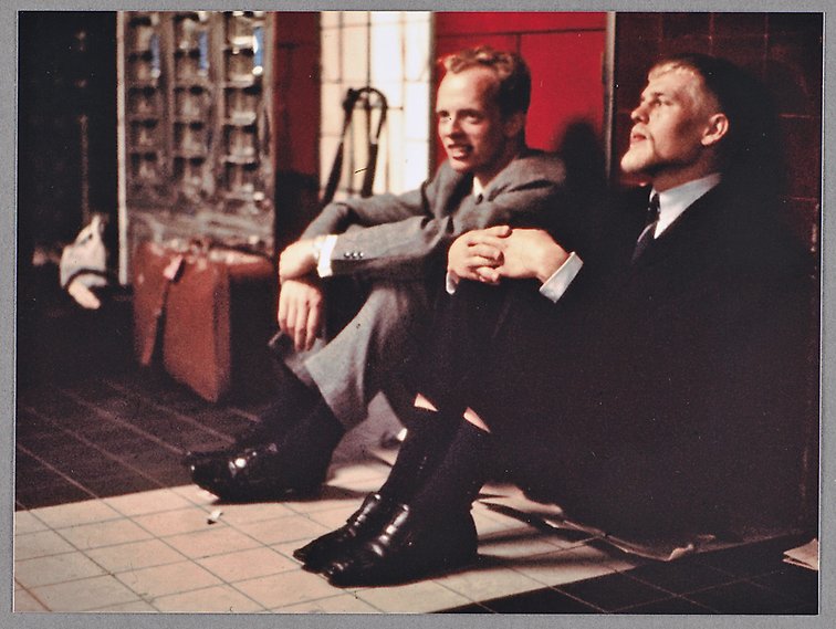 Färgfotografi som föreställer två unga män i kostym och slips som sitter på golvet i tunnelbanan.