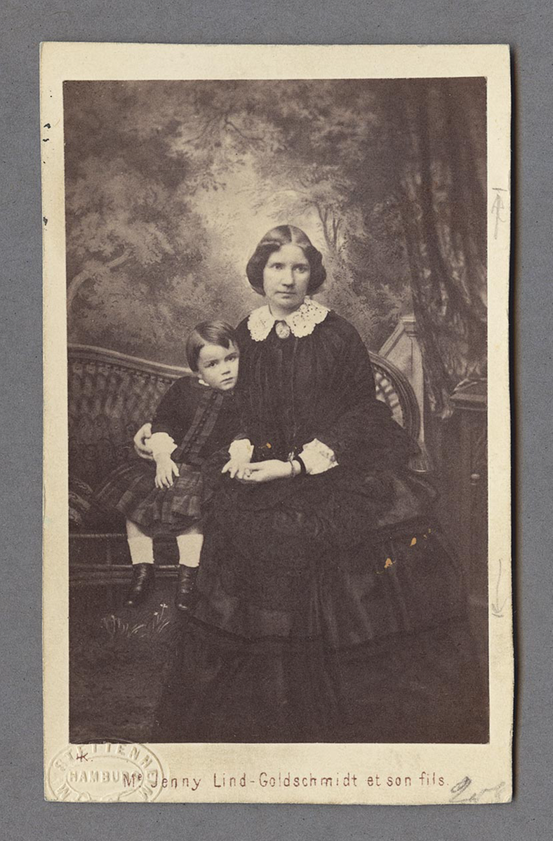 Jenny Lind sitter på en rottingsoffa tillsammans med en liten pojke.